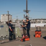 Cold Cloud technicians working on a rooftop HVAC unit with tool bags