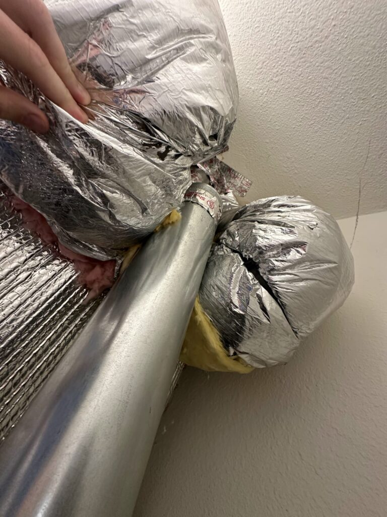 HVAC technician handling insulated attic ductwork during a service visit