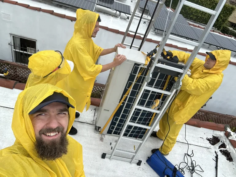 Cold Cloud crew in rain gear installing a heat pump on a rooftop