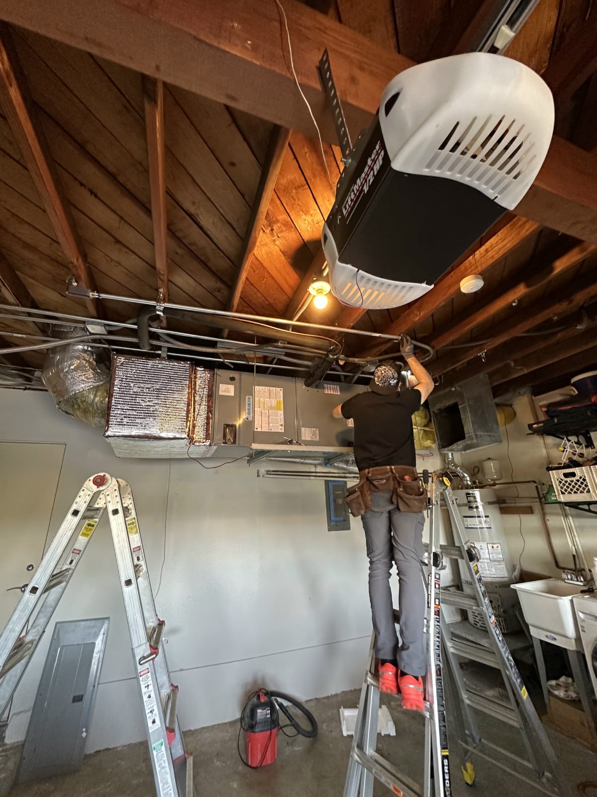 Technician on ladder performing attic HVAC installation work