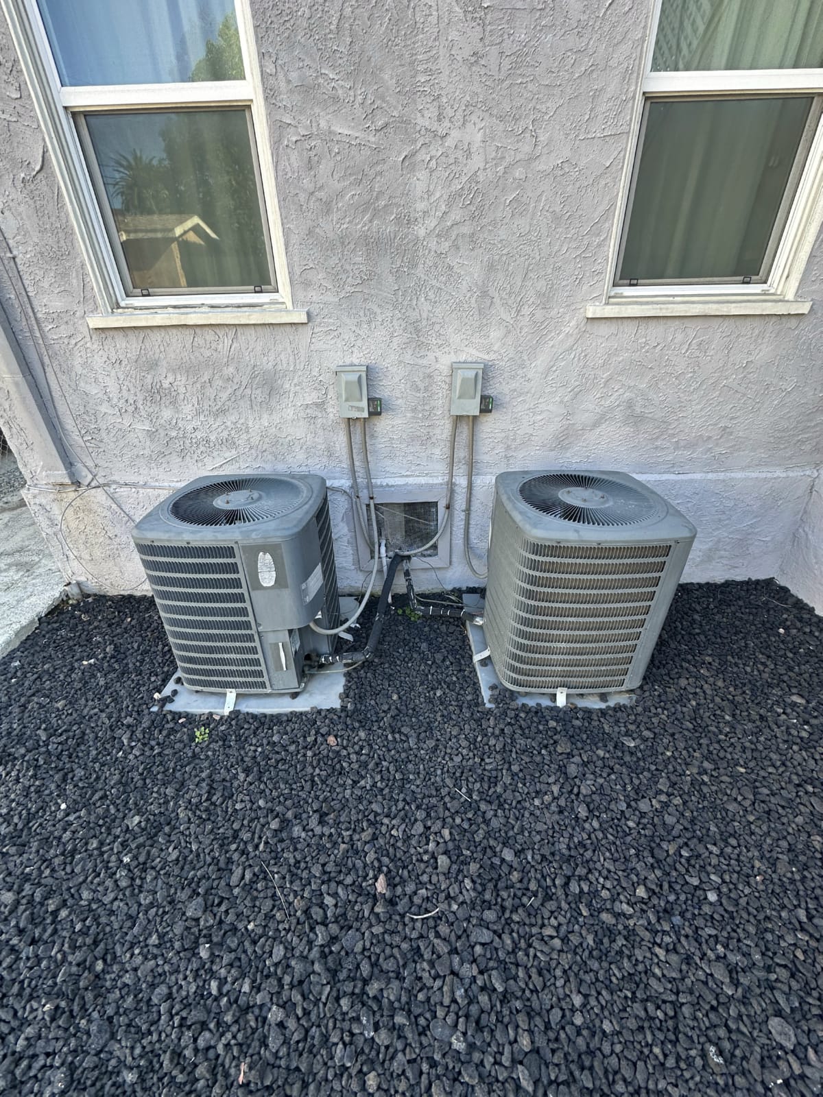Condo HVAC condenser placement meeting HOA siting rules Two outdoor HVAC condenser units placed on shared gravel pad at condo building