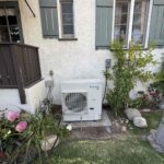 Outdoor heat pump unit installed on concrete pad beside residential home