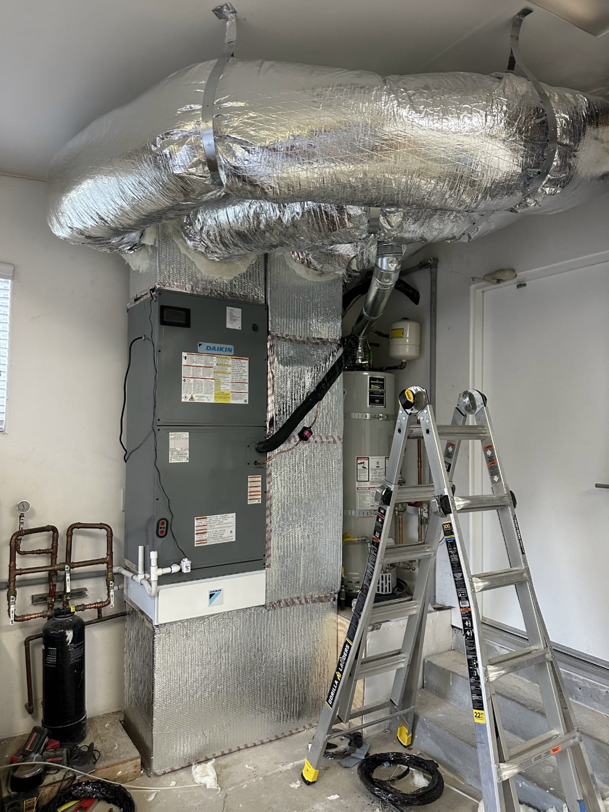 Technician accessing air handler for evaporator coil service HVAC technician servicing equipment from a ladder inside attic installation